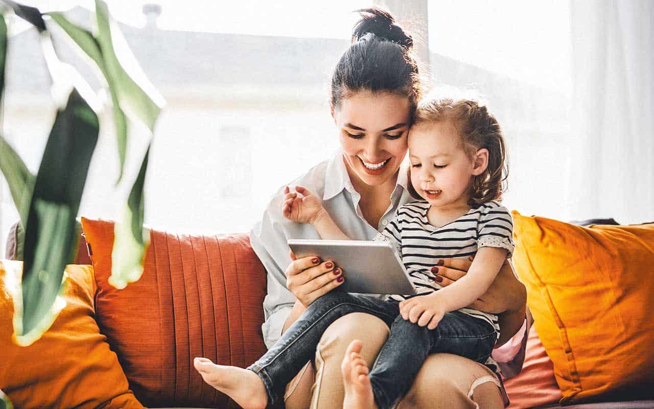 A nanny reads a tablet with a small child | Household Staffing