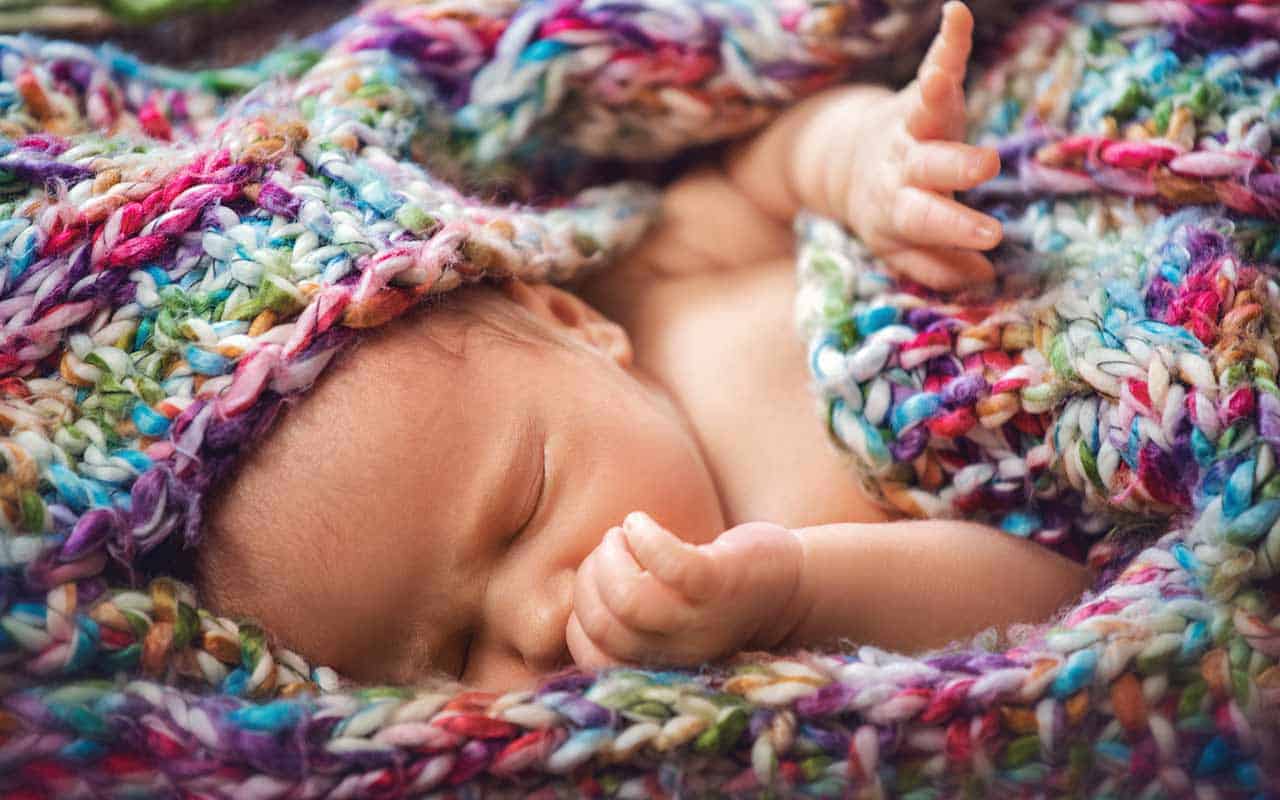 A newborn baby in the care of a newborn care specialist and night nanny is sleeping wrapped in a colorful scarf | Household Stfafing